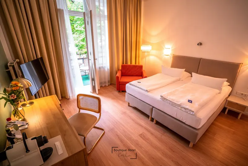 Berliner Balkonzimmer mit Kingsize-Bett, Schreibtisch und geöffneter Balkontür ins Grüne