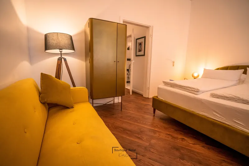 Deluxe Queen mit großem Bett und senffarbenem Sofa als zusätzlicher Sitzmöglichkeit