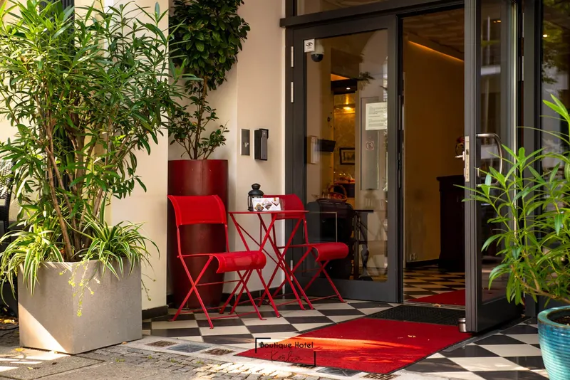 Entrance area of Boutique Hotel Kerlin with large green plants, red bistro chairs and a black-and-white tiled floor
