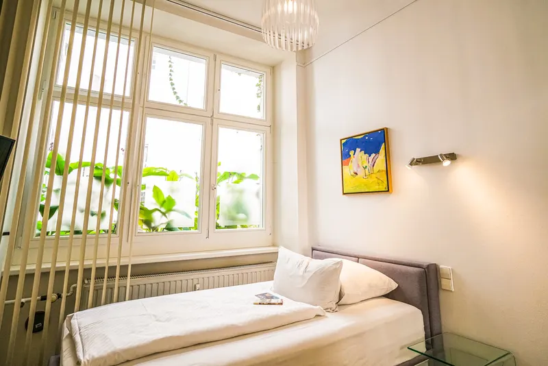 Einzelzimmer im Erdgeschoss mit 1,20-Meter-Bett unter einem großen Fenster mit Blick ins Grüne