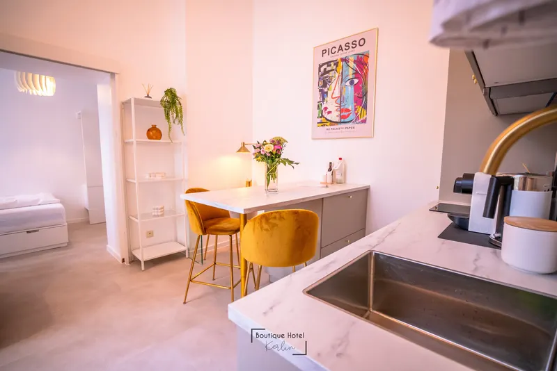 Studio mit Küche: Wohnbereich mit Kücheninsel und gelben Stühlen, dahinter der Schlafbereich
